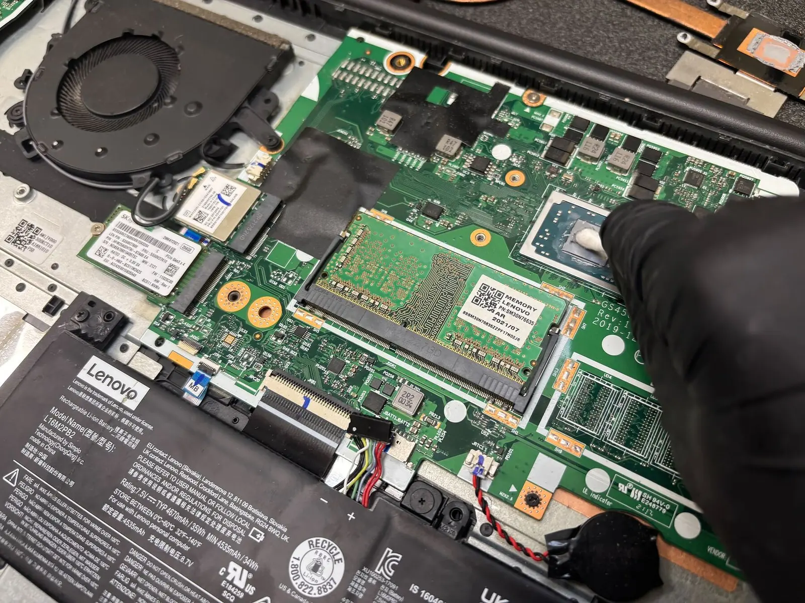 Mano con guanto nero che pulisce il processore di un notebook Lenovo aperto sul banco